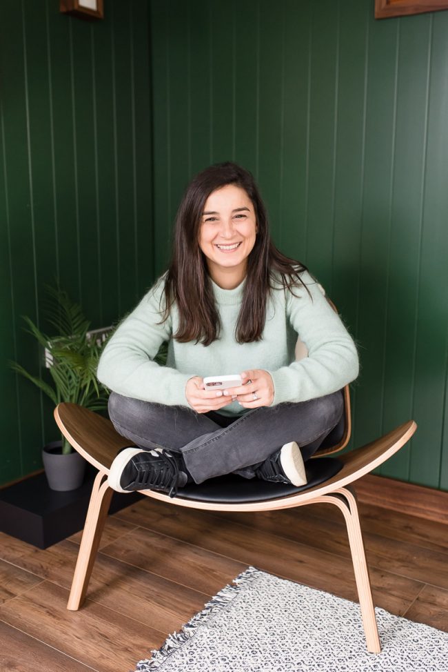 brand sitting on chair cross legged with phone